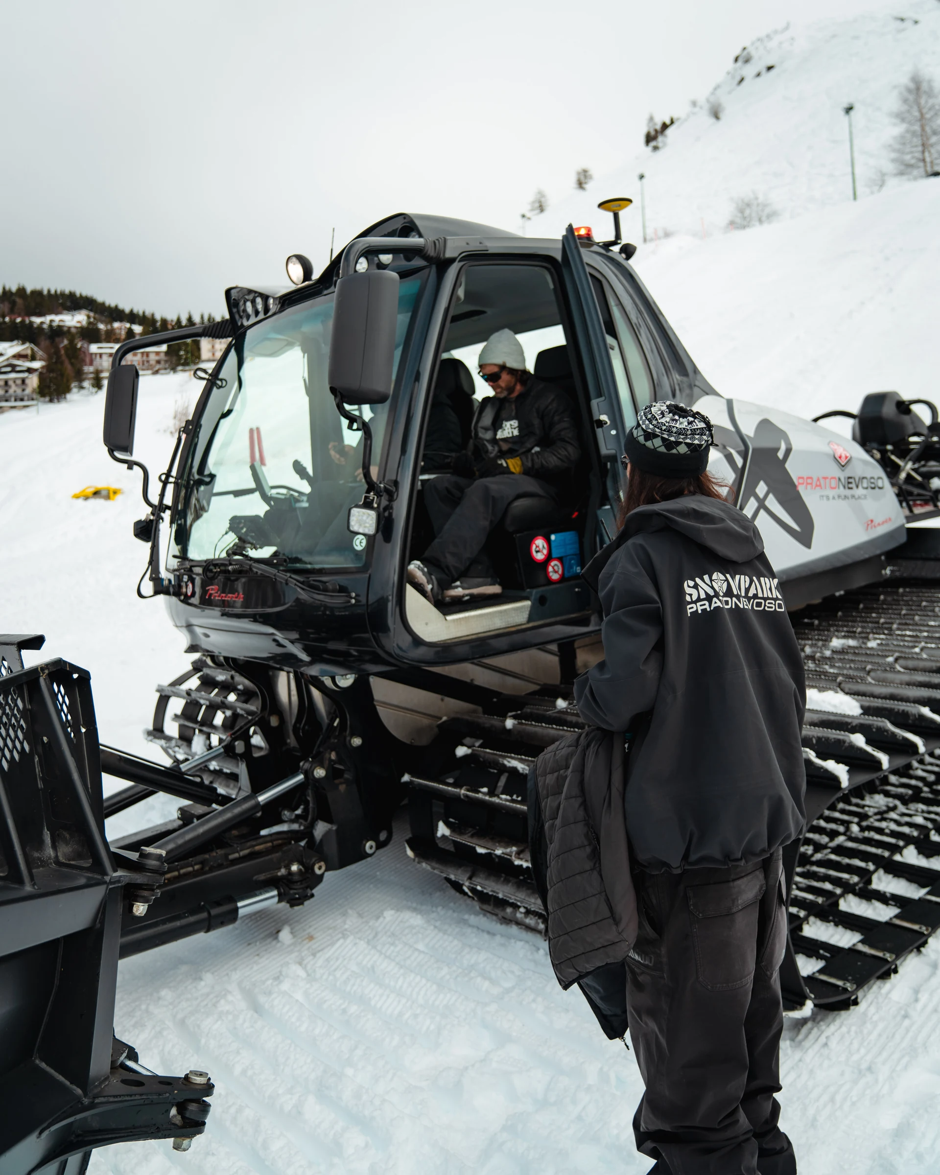 Uno shaper accanto al battipista nello snowpark
