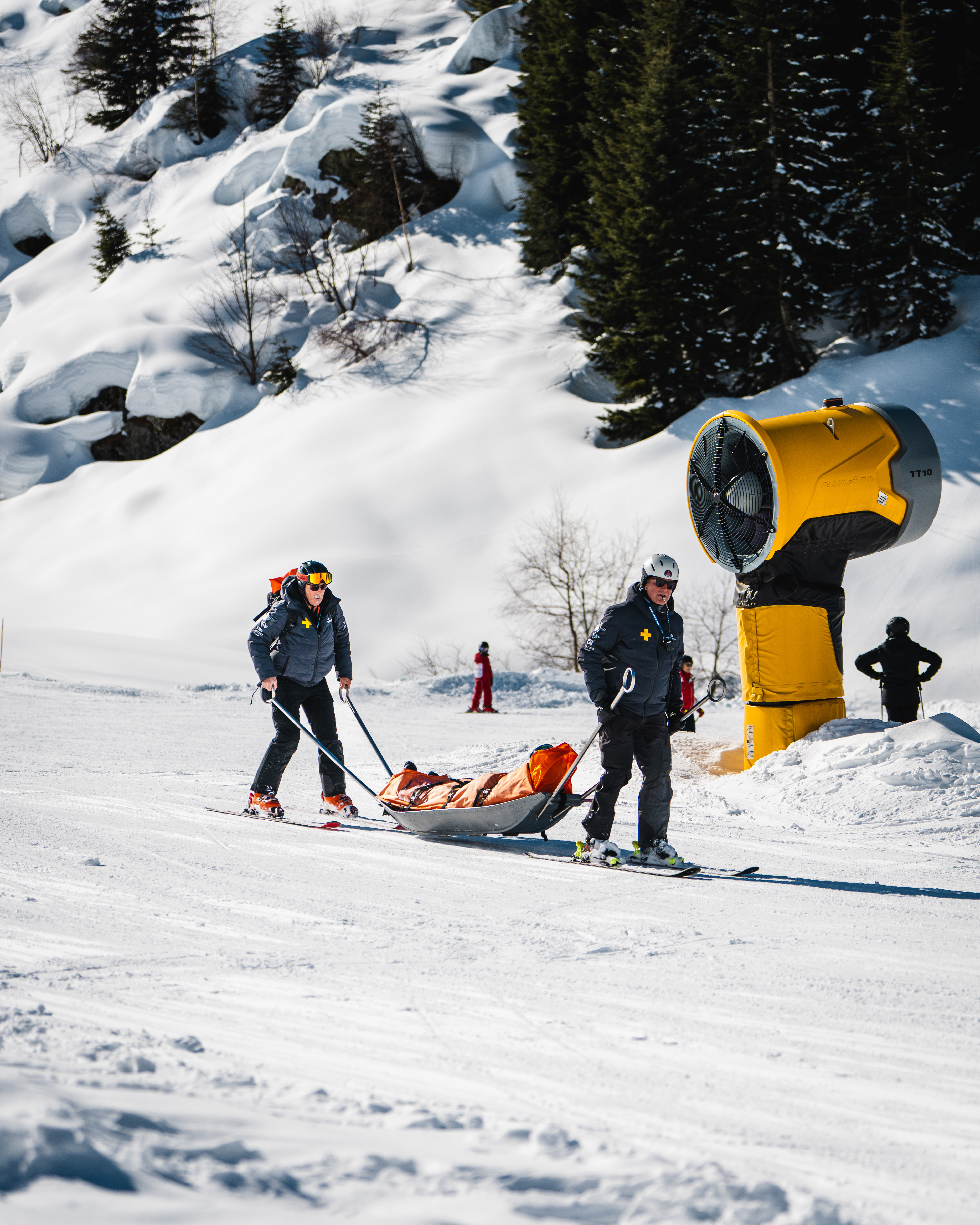 Due addetti al soccorso piste conducono una slitta arancione sulla neve