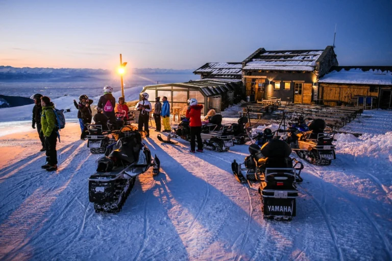 Un gruppo con le motoslitte davanti a uno chalet nella luce del tramonto