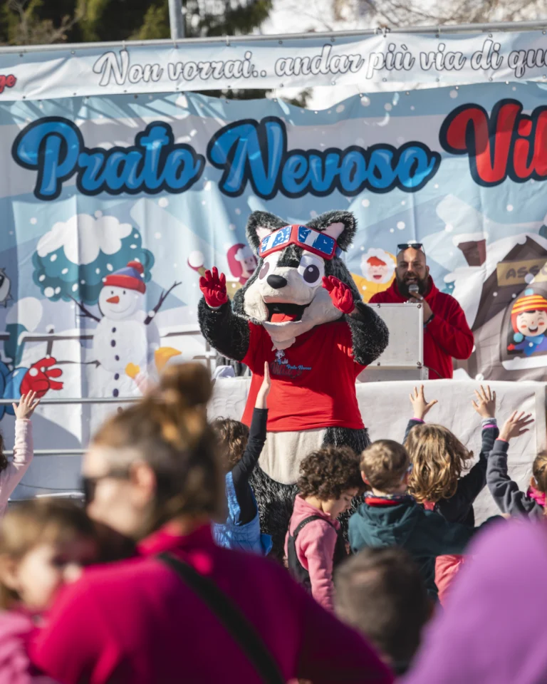 Mascotte in rosso saluta sul palco Prato Nevoso Village davanti ai bambini.