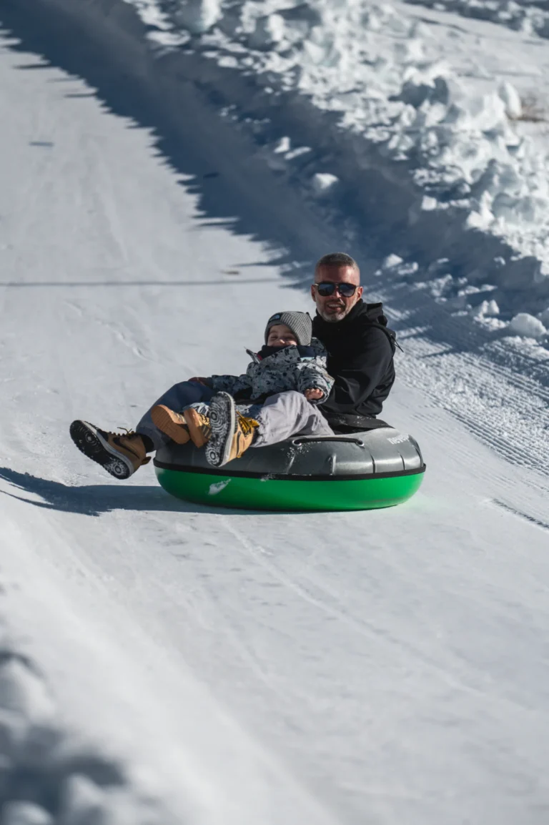 Un adulto e un bambino scendono sulla neve su una ciambella da Snowtubing
