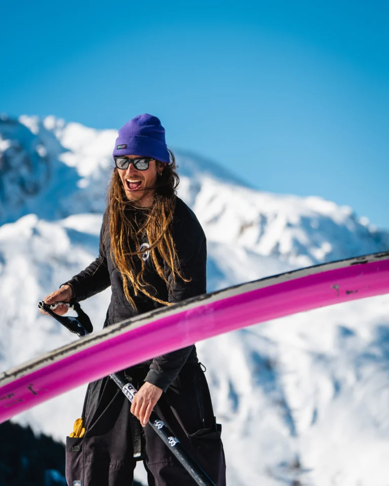 Persona sorridente con dreadlocks porta una tavola snowboard rosa sulla spalla