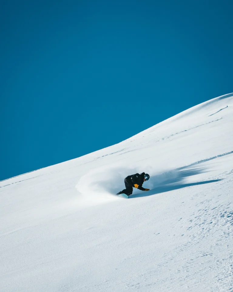Sciatore curva su neve fresca con cielo blu intenso.