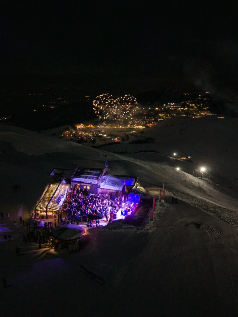 Chalet Il Rosso illuminato di sera, visto dall’alto con il paese sullo sfondo.