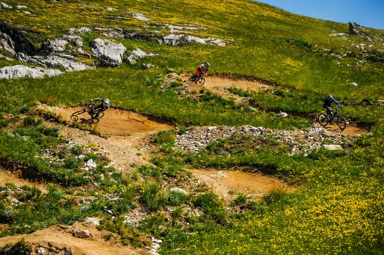 Tre rider affrontano le curve di un tracciato tra i prati del Bikepark di Prato Nevoso