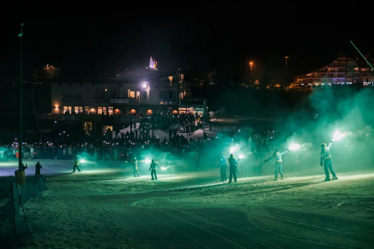 Sciatori con fiaccole illuminate nella Conca di Prato Nevoso durante una fiaccolata serale.