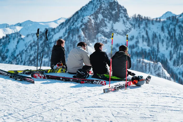 Quattro sciatori seduti sulla neve guardano il panorama delle montagne
