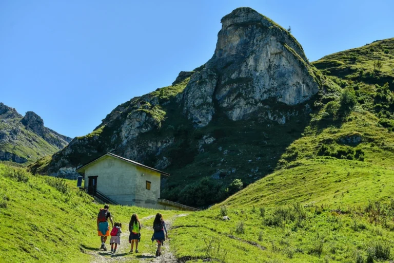 Quattro persone seguono un sentiero tra prati verdi e una formazione rocciosa