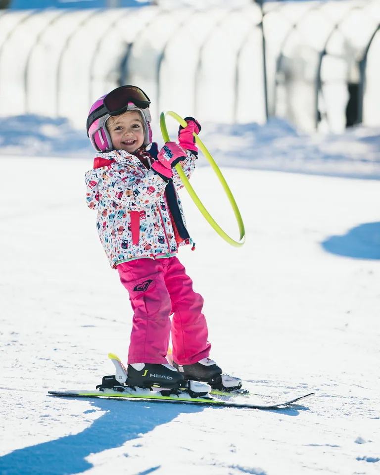 Bambina sorridente sui piccoli sci, con casco rosa e cerchio giallo