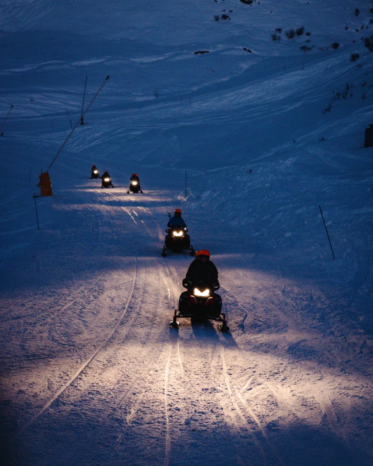 Motoslitte in fila sulle piste innevate al calare della sera.