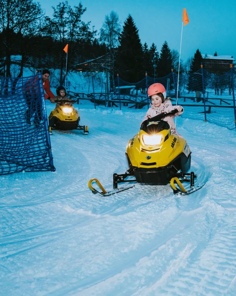 Bambina con casco rosa alla guida di una mini motoslitta gialla.
