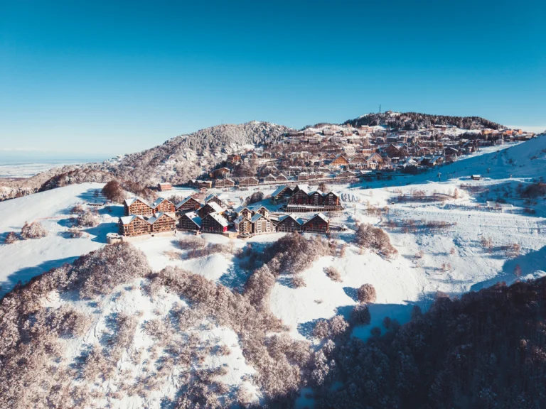 Veduta aerea di Prato Nevoso e degli chalet di Stalle Lunghe circondati dalla neve, sotto un cielo azzurro.