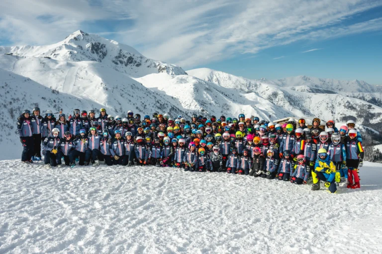 Grande gruppo in abbigliamento sci disposto davanti alle montagne innevate.