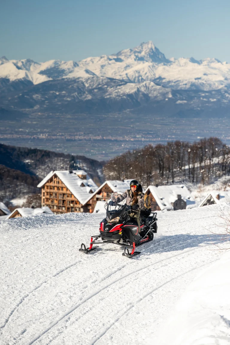 Persona su motoslitta sulla neve con chalet e montagne.