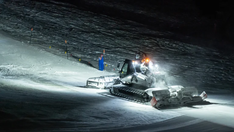 Gatto delle nevi illuminato sulle piste durante una serata sulla neve.
