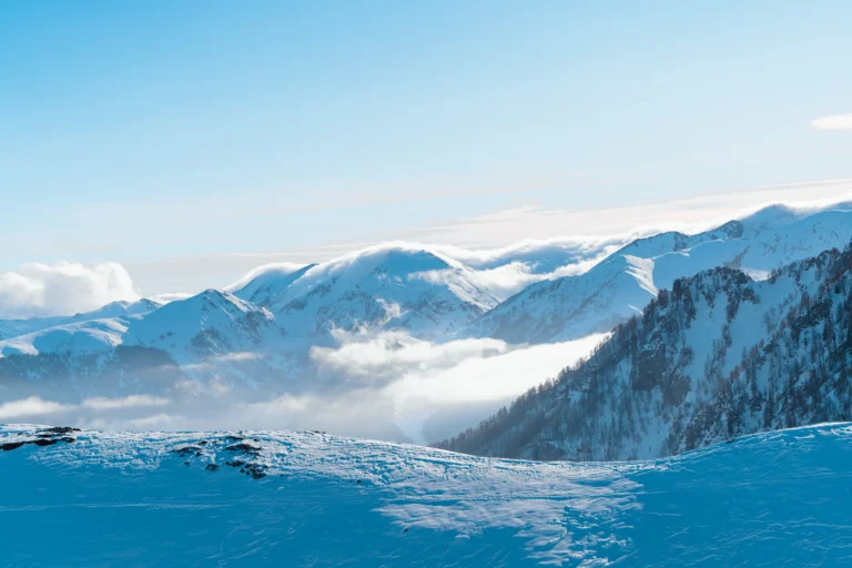 Veduta panoramica larga di montagne innevate e nuvole basse al sole.