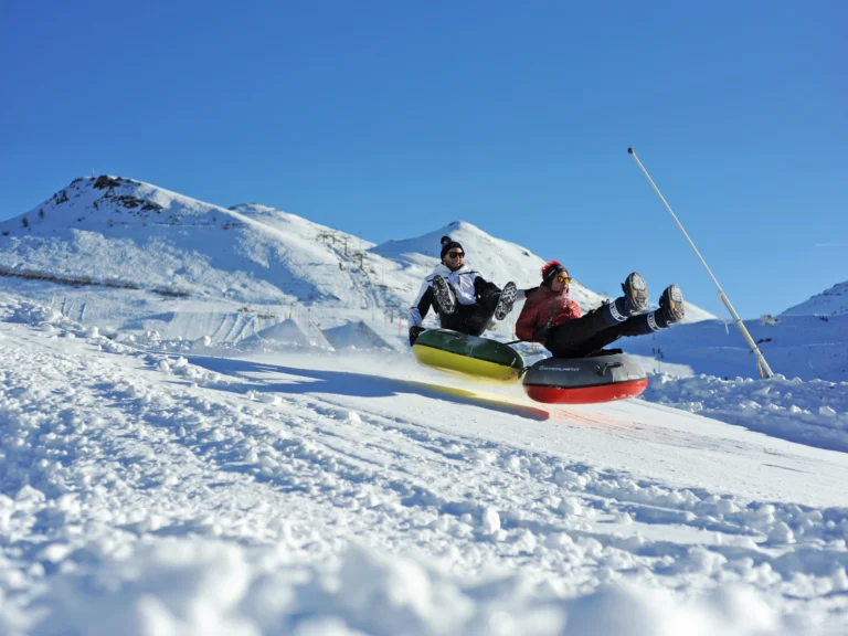 Due persone scendono con i gommoni sulla neve, davanti alle montagne.
