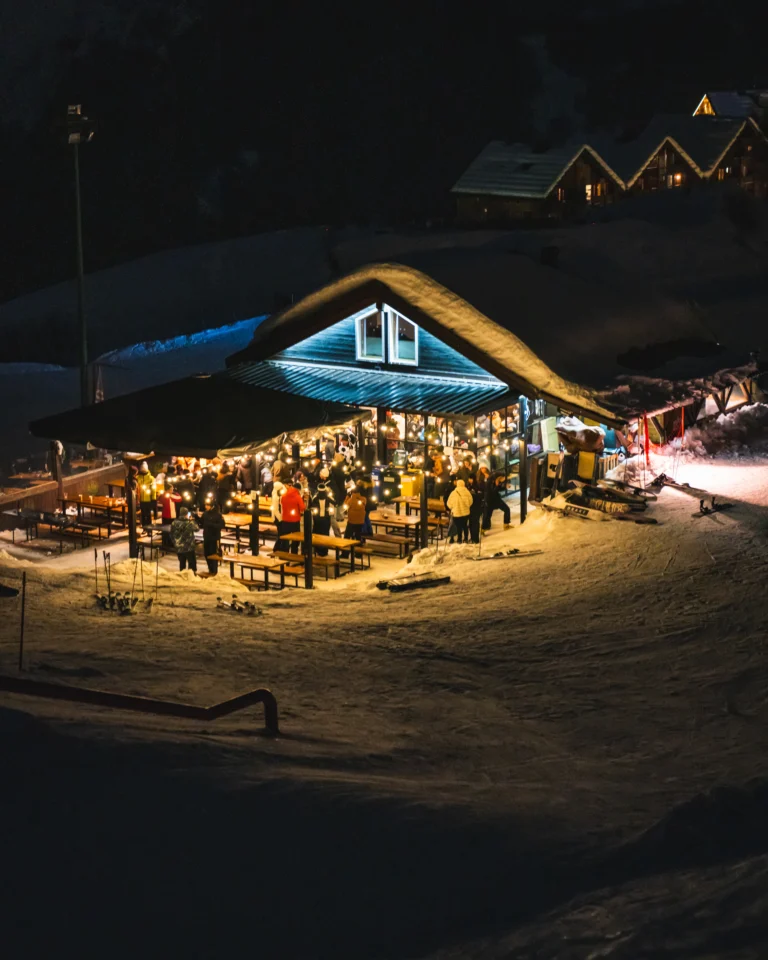 Chalet illuminato di luci calde con persone all'aperto nella notte.