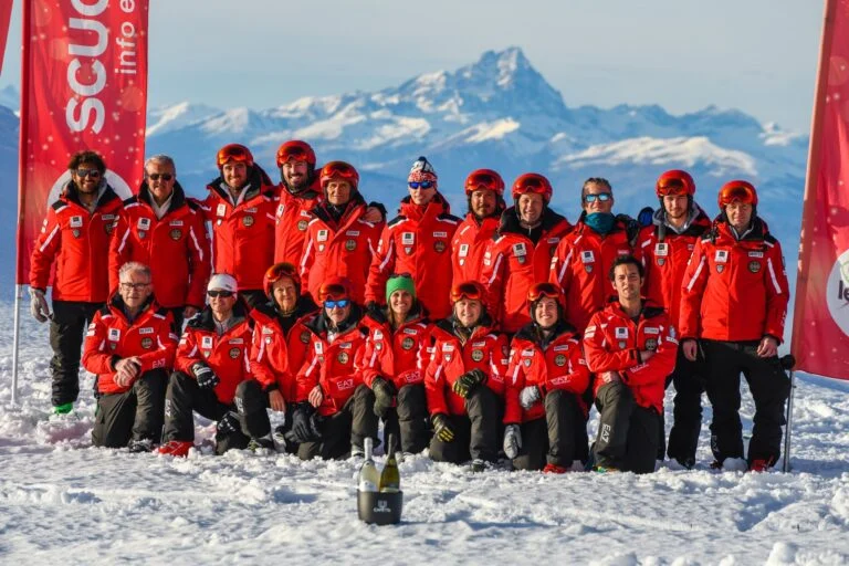 I maestri di Ski Leader in divisa rossa, in posa sulla neve con le Alpi sullo sfondo