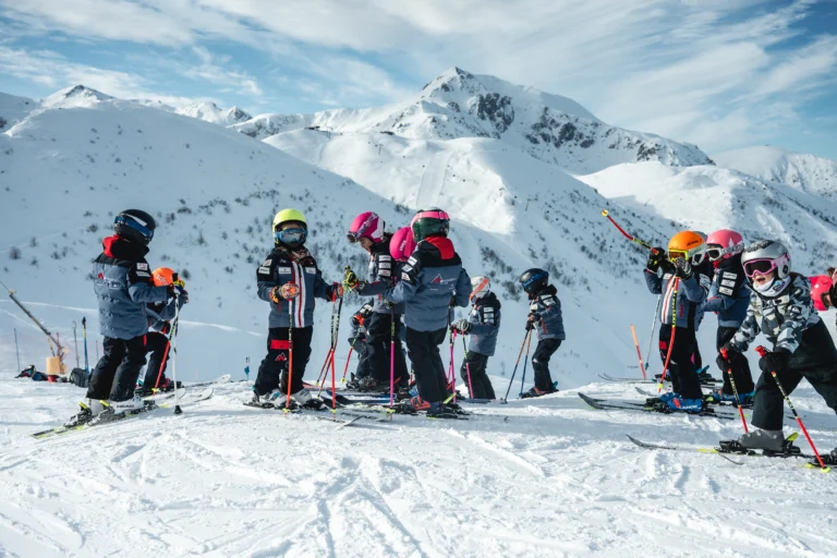 Gruppo di bambini con sci e caschi colorati davanti alle montagne.
