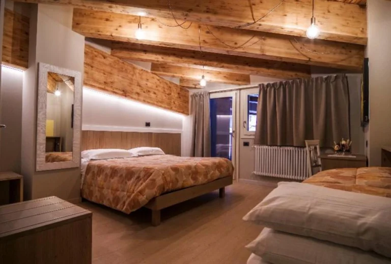 Una camera dell’Hotel Laghetto con travi in legno, letto matrimoniale e letti singoli