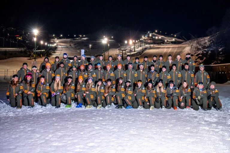 I maestri di Snow Academy in divisa, riuniti di sera sulla neve con le piste illuminate alle spalle
