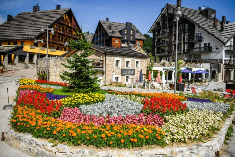 La piazzetta fiorita di Stalle Lunghe in estate, tra facciate in pietra e chalet in legno