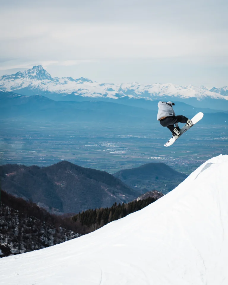 Snowboarder in salto sopra pendio con panorama montano lontano.