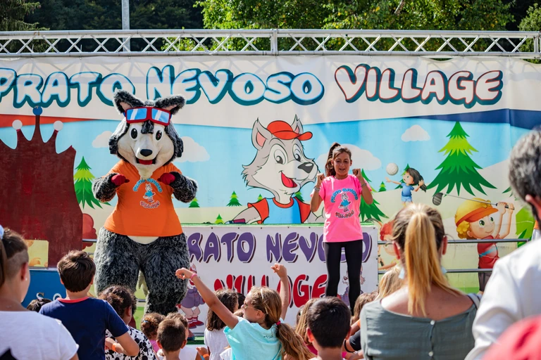 Asso e un’animatrice sul palco estivo del Village, con bambini e adulti davanti a loro