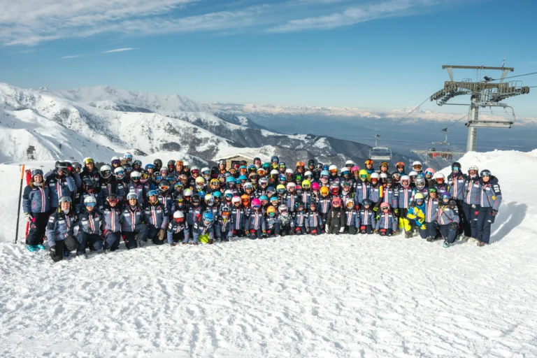 Foto di gruppo degli atleti e dei tecnici del Mondolé Ski Team sulle piste, con le montagne e la seggiovia alle spalle.