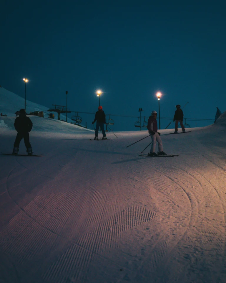 Sciatori sulle piste illuminate al calare della sera.