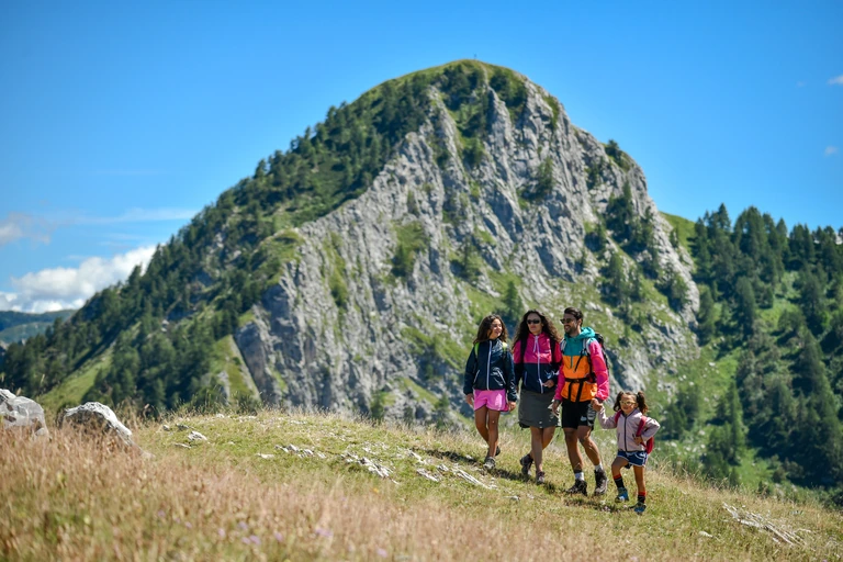 Quattro persone camminano tra i prati, sotto una grande parete rocciosa
