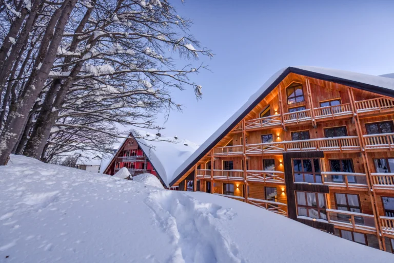 Chalet Everest tra la neve e gli alberi, con la facciata in legno e i balconi illuminati.