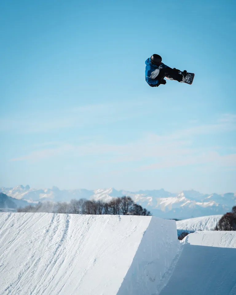 Snowboarder in salto sopra una rampa innevata, con cielo azzurro