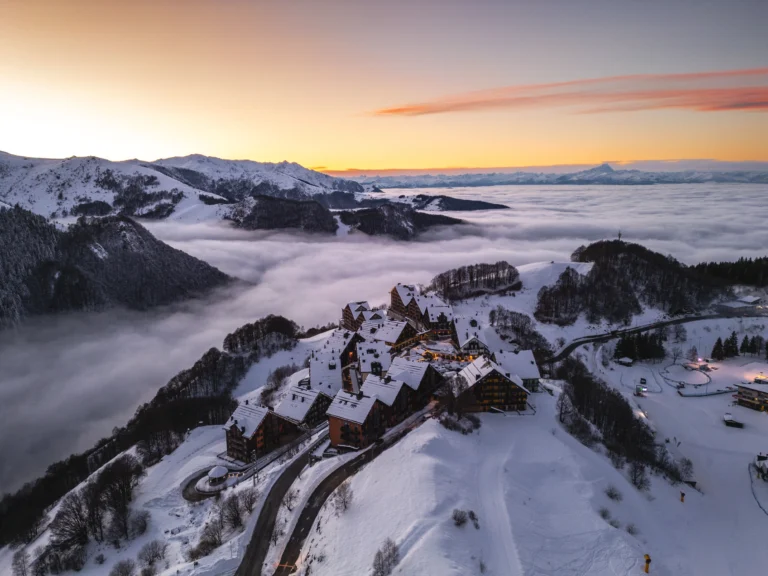 Il borgo di Stalle Lunghe innevato al tramonto, tra le montagne e un mare di nuvole.