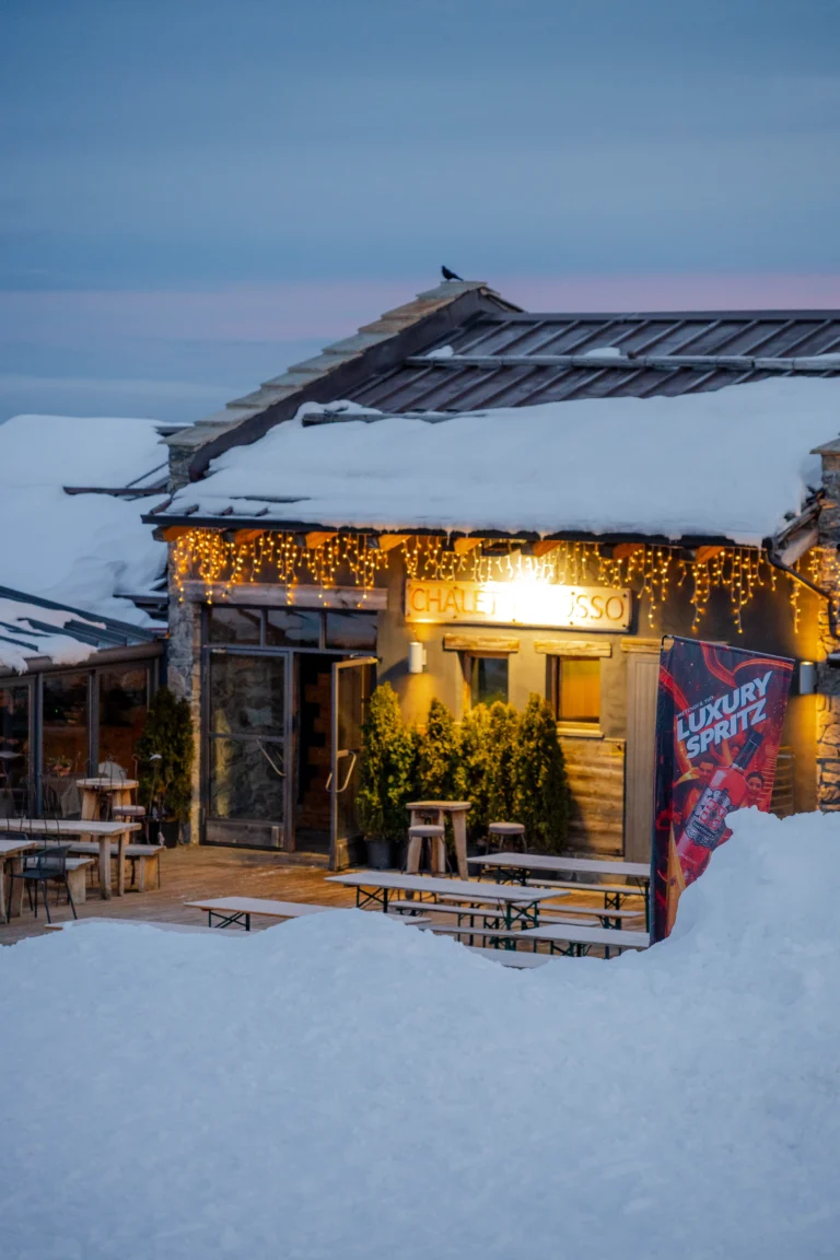Chalet Il Rosso innevato con luci accese sulla facciata alle prime luci del giorno.