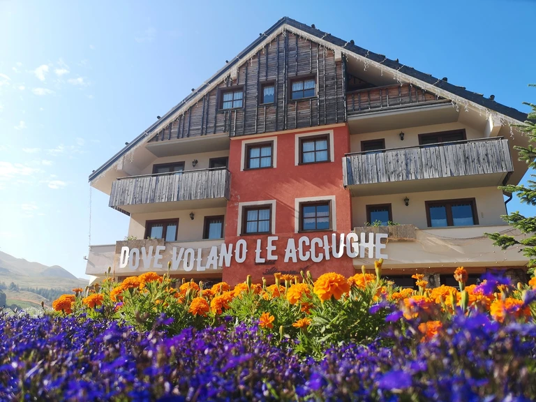 Facciata con insegna Dove volano le acciughe, fiori colorati e cielo azzurro