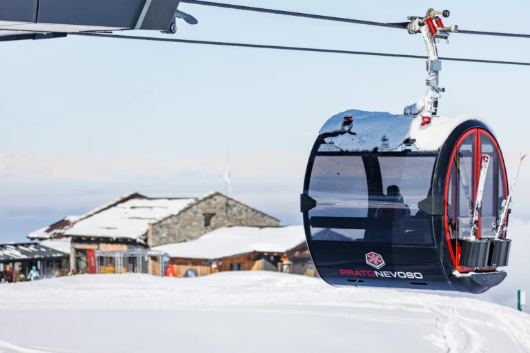 Cabina della telecabina La Rossa con gli sci all’esterno, davanti agli edifici innevati in quota.