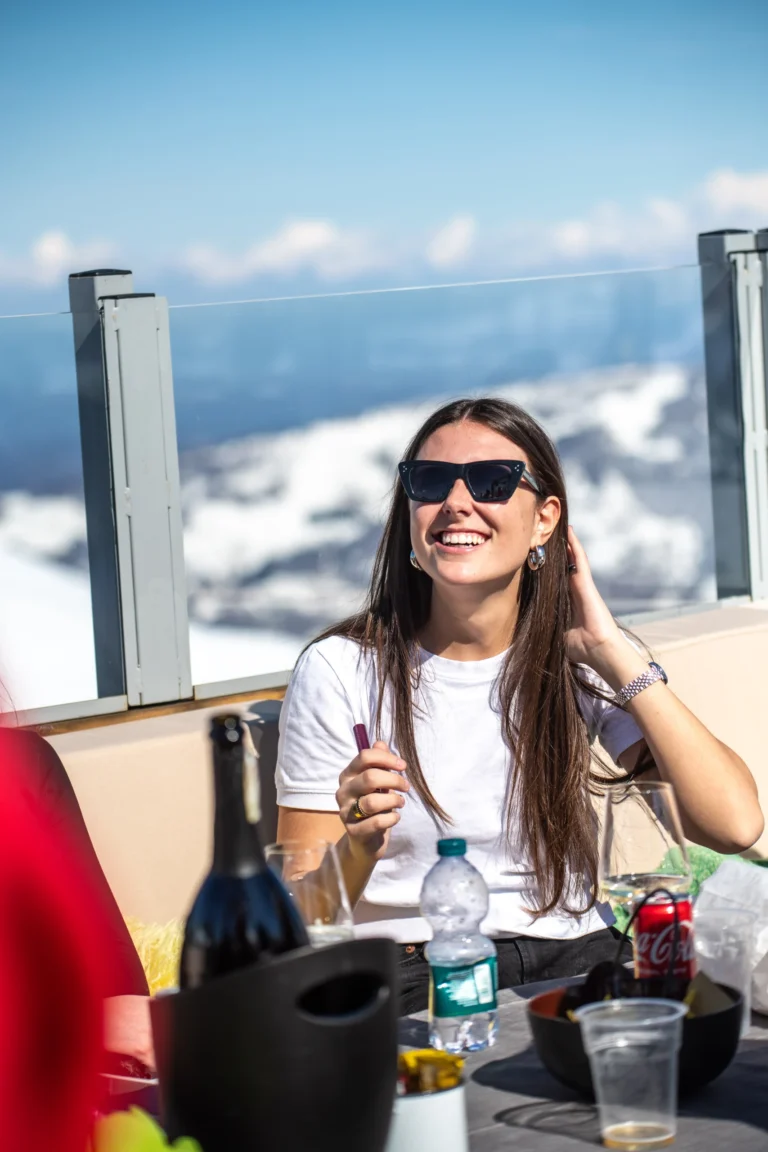 Una donna con un calice al tavolo all’aperto, con le montagne innevate sullo sfondo