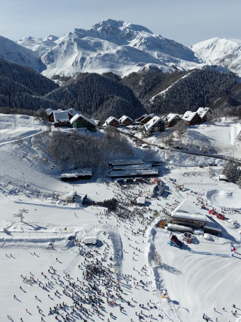 Veduta aerea della Conca e del paese innevato di Prato Nevoso, con le montagne sullo sfondo.