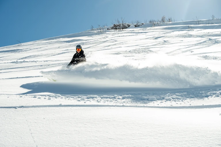 Sciatore con maschera arancione in una curva nella neve fresca al sole
