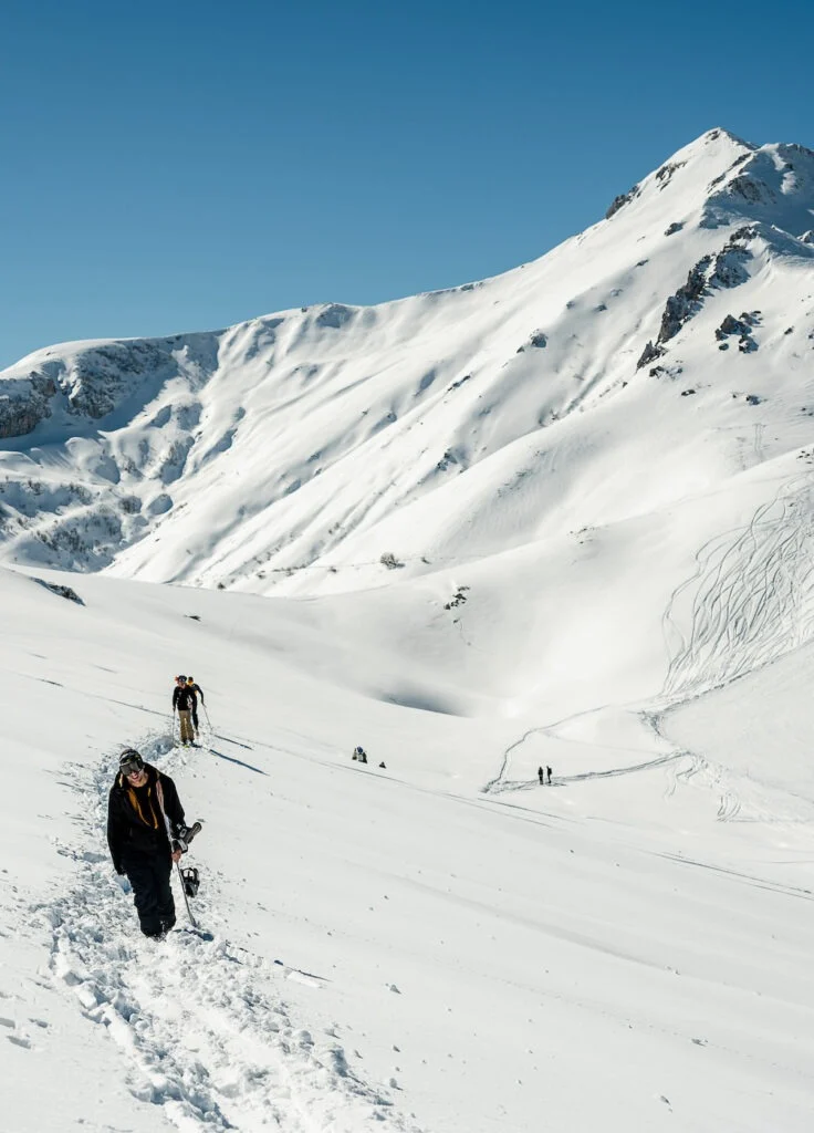 Due persone risalgono un ampio pendio innevato, lontano dalle piste