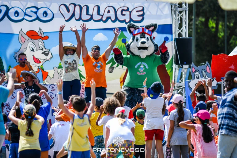 Bambini alzano braccia davanti ad animatori e mascotte lupo Village.