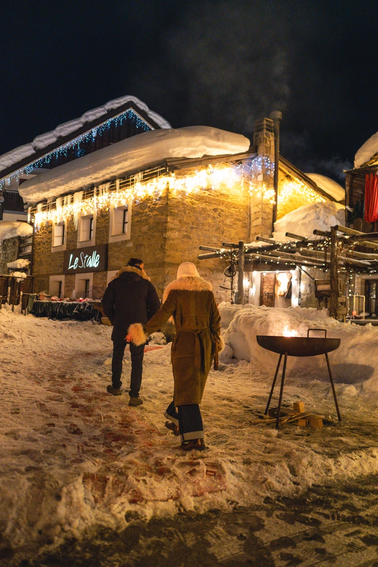 Due ospiti davanti all’Osteria Le Stalle, tra neve, luci e un braciere