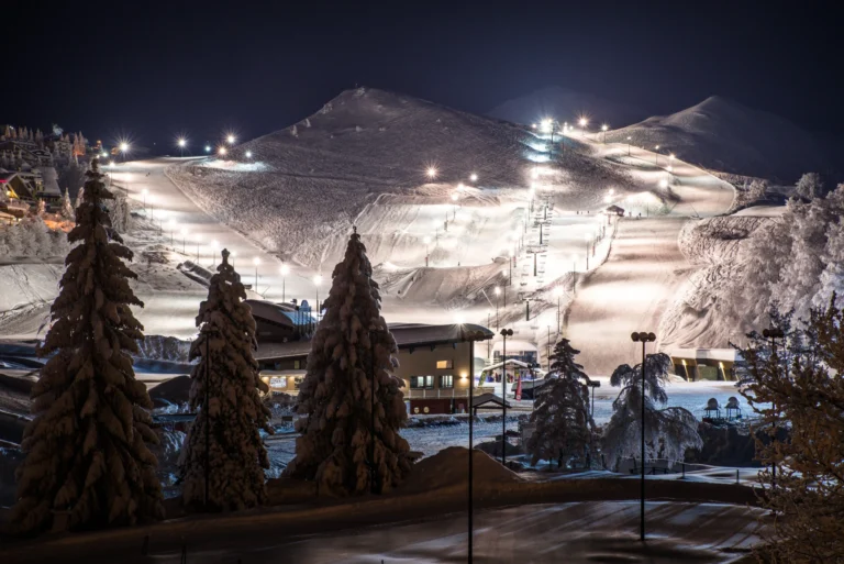 Panorama delle piste illuminate di Prato Nevoso con alberi innevati in primo piano.