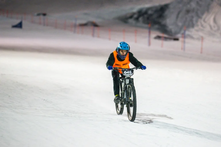 Ciclista con casco azzurro procede frontalmente sulla neve illuminata.