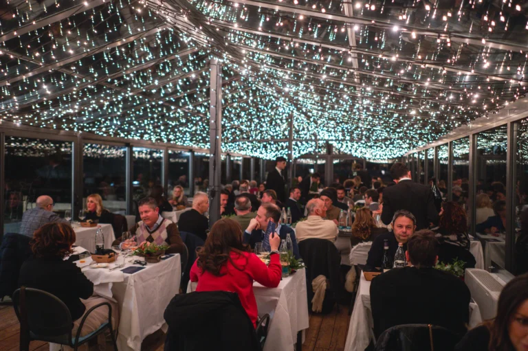 Ospiti a cena nella sala vetrata dello Chalet Il Rosso, sotto il soffitto illuminato da tante piccole luci.