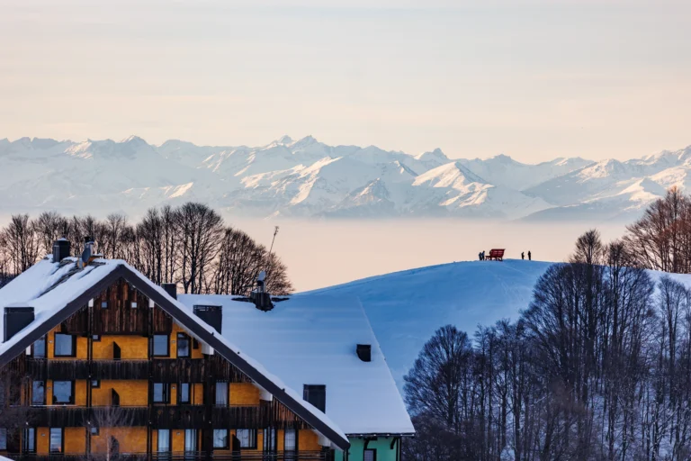 Chalet innevato davanti alle montagne al tramonto.